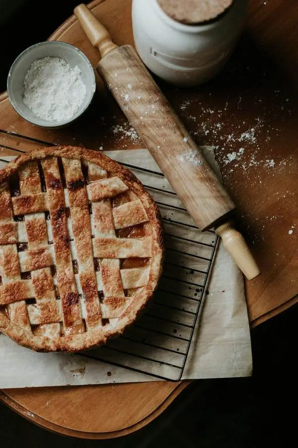 Tarte aux pommes au croisillon de pâte dorée, à côté d’un rouleau à pâtisserie fariné